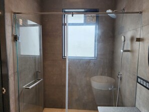 A modern bathroom with a glass-enclosed shower, a visible window, a sink, and a showerhead.