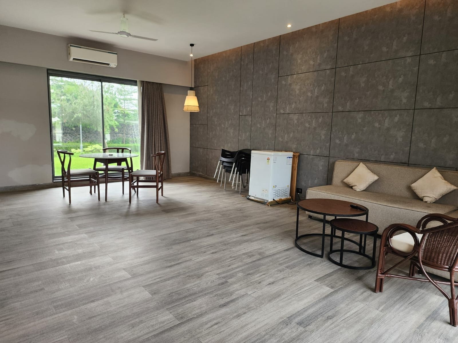 A modern interior with a dining area, sofa, and a view of greenery outside.
