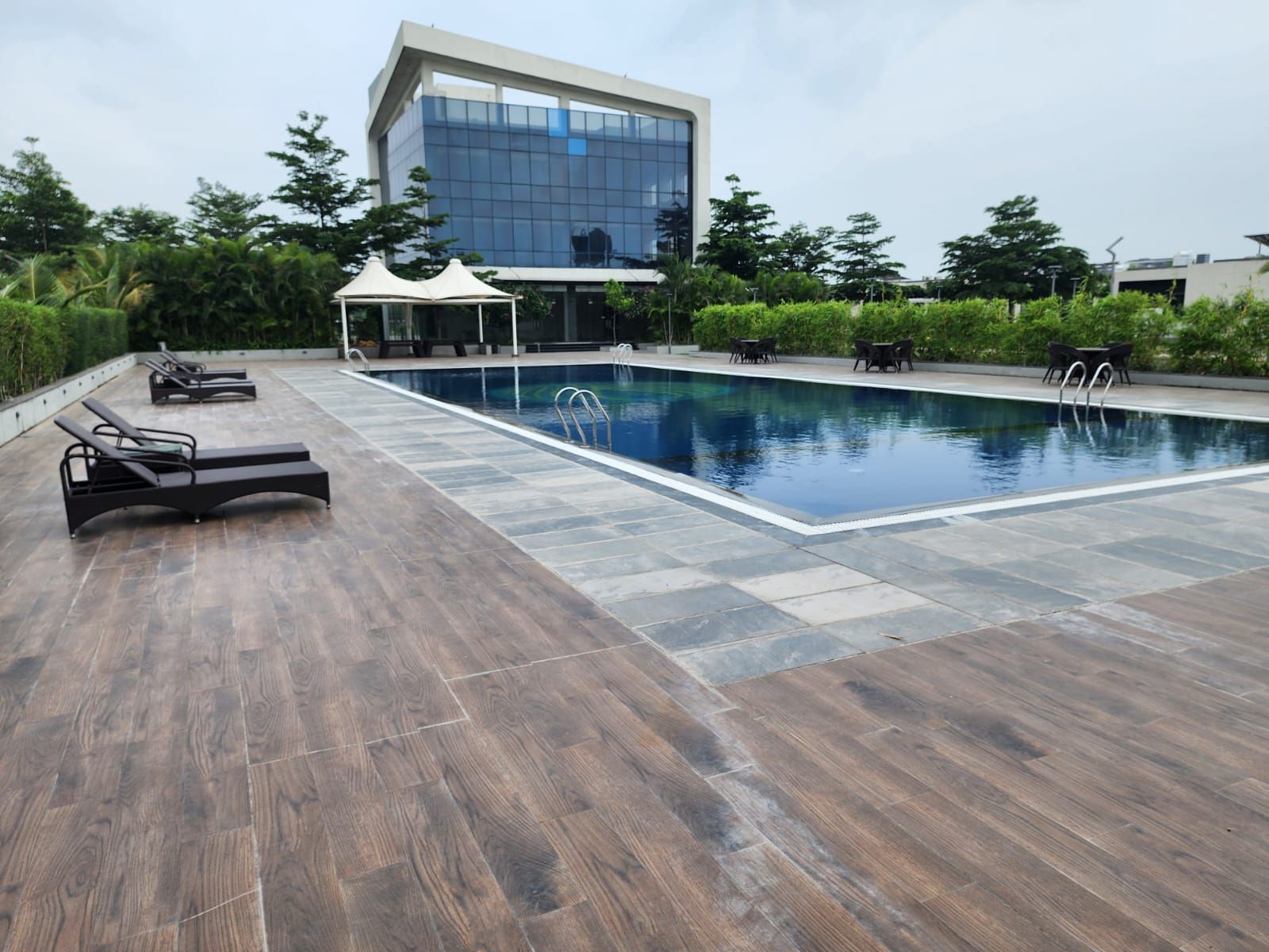 Una piscina con sillones de descanso y un edificio moderno al fondo.