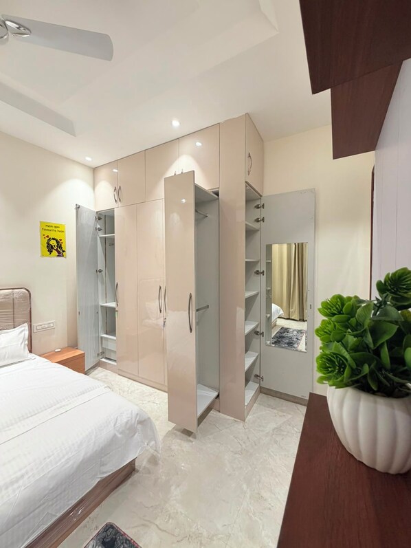A bedroom with a bed, a wardrobe, a mirror, and a potted plant.