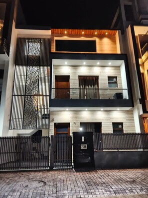 A modern two-story building with a black metal fence, a wooden staircase, and a garage with a number plate.