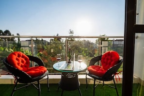 A balcony with two chairs and a table, a glass partition, and a view of greenery. - Elite suites near all embassies (ruaka cytonn)