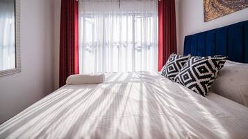 A hotel room with a bed, a window with sheer curtains, a headboard, and a wall-mounted artwork.