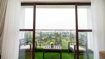 A balcony with a table and chairs, a view of a cityscape, and a green lawn.