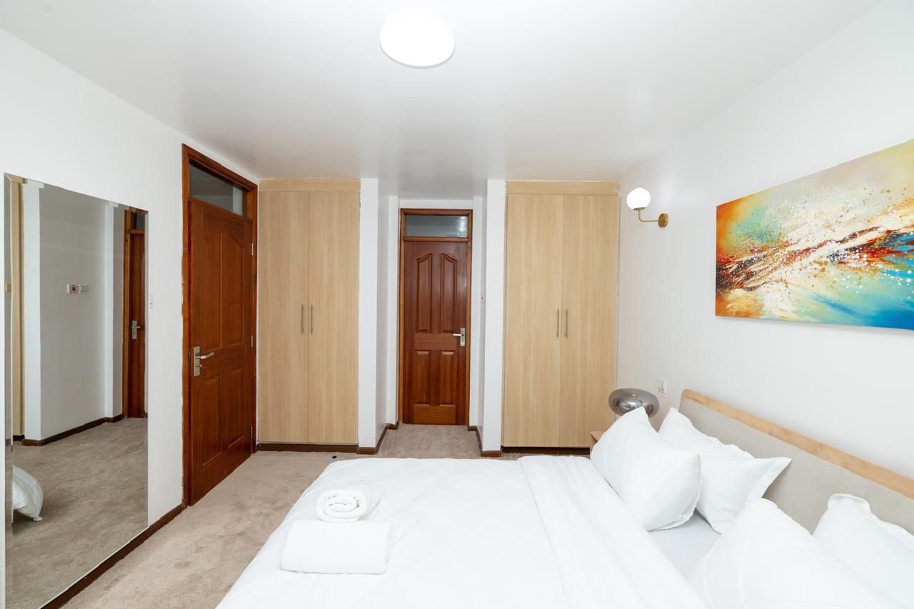 Quarto de hotel com cama, quadro na parede e porta para outro cômodo.