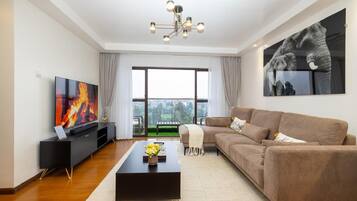 A modern living room with a flat-screen TV, a black entertainment unit, a brown sofa, a coffee table, and a large window with a view.