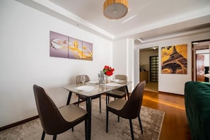 A dining area with a table set for two, a vase with red flowers, and artwork on the wall. - Elite suites near all embassies (ruaka cytonn)