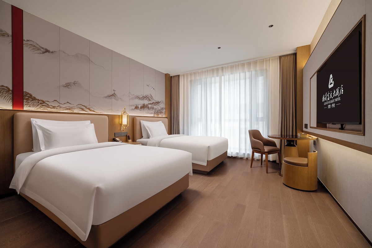 Habitació d'hotel amb dos llits, escriptori, cadira, televisió i una paret decorada amb obres d'art.