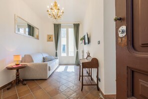 A room with a sofa, a small table with a lamp, a wooden bench, a mirror, a chandelier, and a door. - Finestra sulle Porte Palatine by Wonderful Italy (Torino)