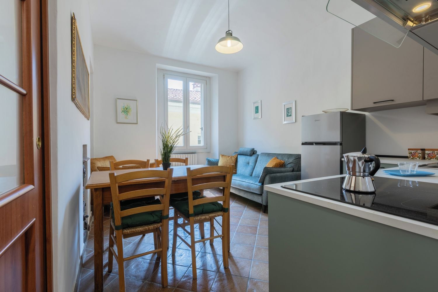 A modern kitchen with a dining area, a sofa, and a window.