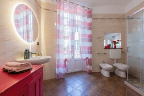A bathroom with a red vanity, a large mirror, a shower with a striped curtain, two toilets, and a glass-enclosed shower area. - Finestra sulle Porte Palatine by Wonderful Italy (Torino)