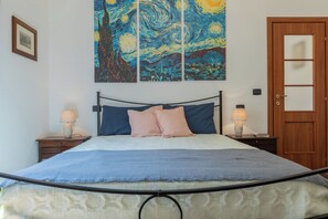 A bedroom with a bed, two bedside tables, a nightstand, a wooden door, and a painting on the wall. - Finestra sulle Porte Palatine by Wonderful Italy (Torino)
