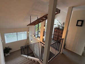 En trappe med gelænder i træ fører op til en balkon med hængende lyspærer.