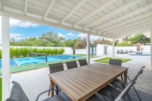 A covered outdoor area with a pool, a dining table with chairs, and a view of the surrounding landscape. - PV Getaway: Heated Pool and Private Pickleball! (Paradise Valley)