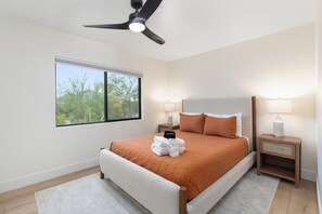 A bedroom with a bed, a ceiling fan, bedside lamps, a window, and a view of trees. - PV Getaway: Heated Pool and Private Pickleball! (Paradise Valley)