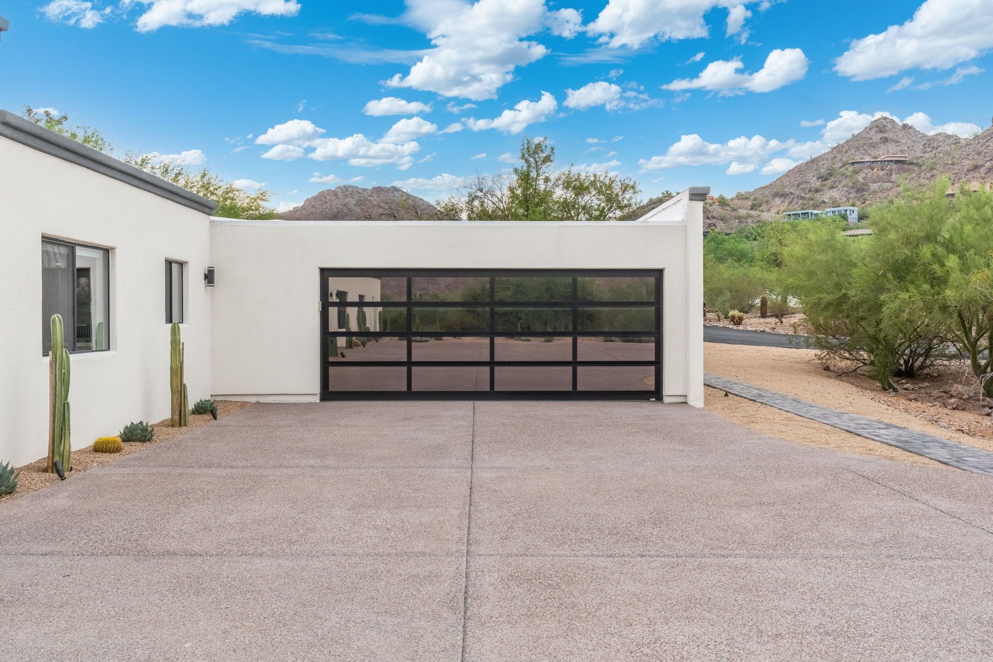 A modern house with a garage, a paved driveway, and desert vegetation.