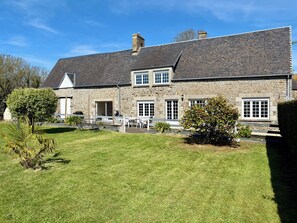 A stone building with a sloped roof, a front door, and a small porch with chairs. - My Little Farmhouse: A Quiet Family Home with an Enclosed Garden - 1.5 km from the sea 🌊 (Dragey-Ronthon)