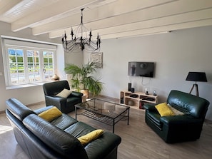A modern living room with leather sofas, a glass coffee table, a chandelier, a television, and a potted plant. - My Little Farmhouse: A Quiet Family Home with an Enclosed Garden - 1.5 km from the sea 🌊 (Dragey-Ronthon)