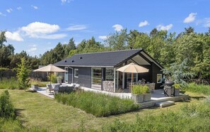Ein modernes Haus mit einer Terrassenfläche, Gartenmöbeln und einem Kamin aus Stein.