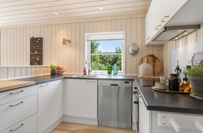 A modern kitchen with white cabinetry, a dishwasher, and a window with a view of greenery.