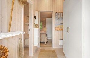 A wooden interior hallway leading to a bedroom with a bed and a poster on the wall.
