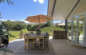 Eine Außenpatio mit Holztisch und -stühlen, einem großen Sonnenschirm und einer Glasdoor, die auf eine Terrasse führt.