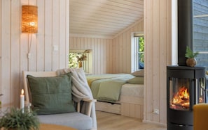 Ein gemütliches Zimmer mit einem Bett, einem Sessel, einem Tisch und einem Kaminofen.