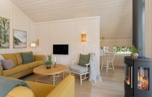 A cozy living room with a sofa, armchair, and a table, a flat-screen TV, and a wood-burning stove.