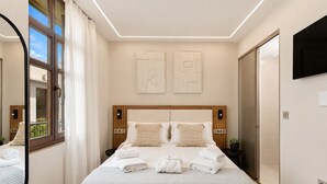 A hotel room with a large bed, two bedside tables, a mirror, and artwork on the wall. - Asikiko Suites - Rethymno Old Town Balcony Suite (Rethymno)