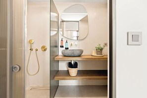 Ein Badezimmer mit einem Steintonne, einem Spiegel, einer Dusche mit goldfarbener Duschbrause und einer kleinen Pflanze auf der Ablagefläche.