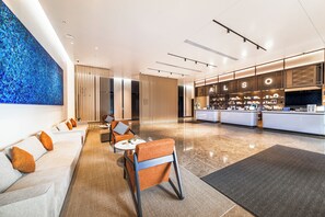 A modern hotel lobby with a reception desk, seating area, and a large abstract art piece on the wall.