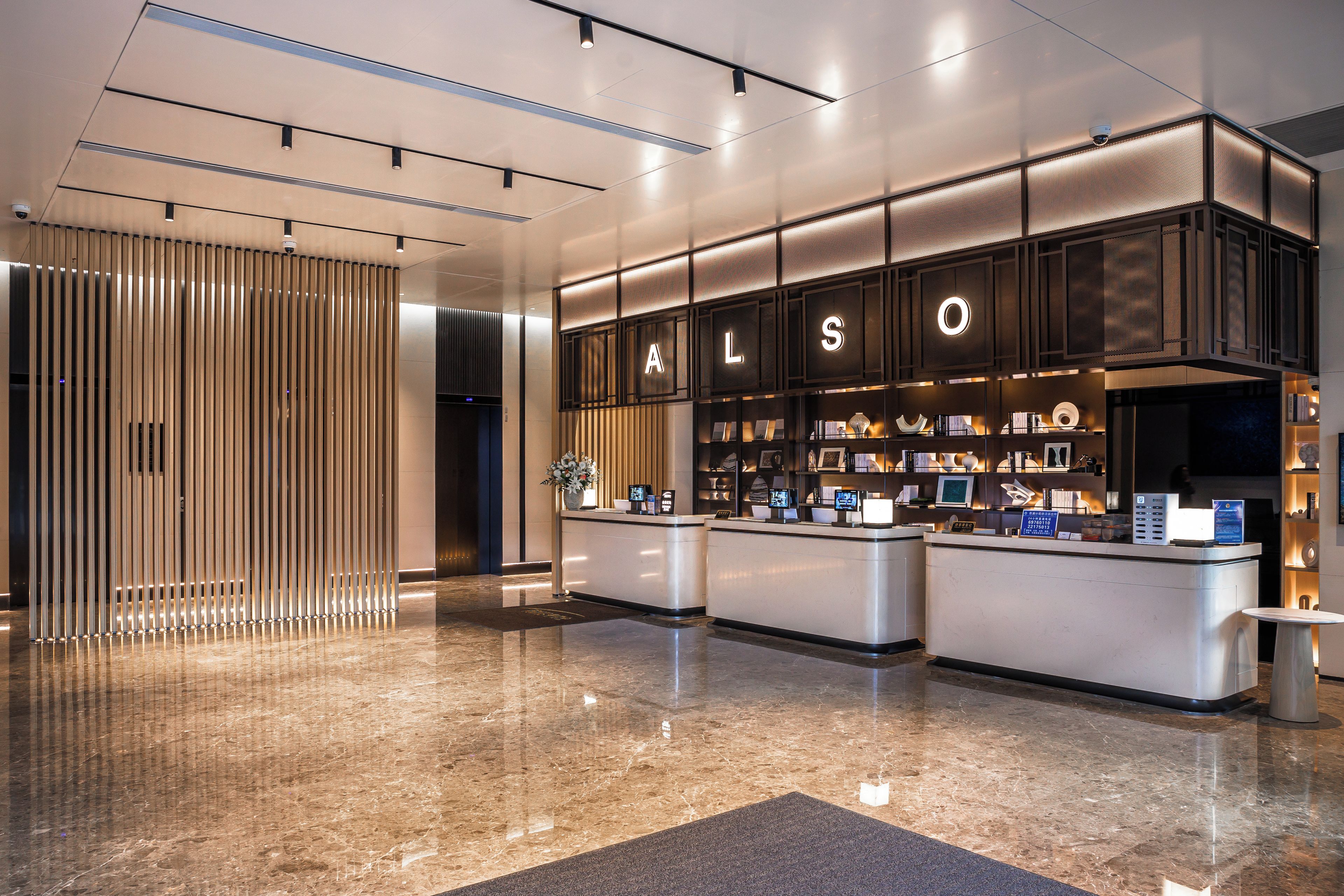 Un área de recepción de hotel con diseño moderno, que incluye un mostrador de recepción, un panel de madera vertical y un interior bien iluminado.
