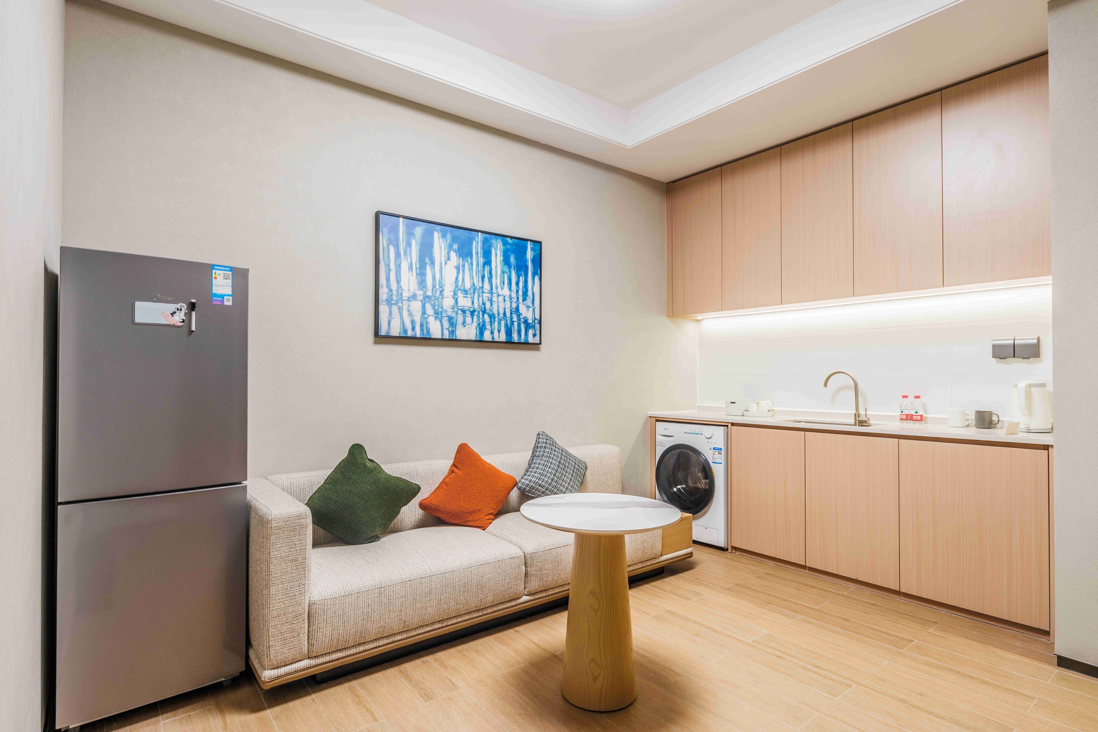 Una kitchenette moderna con lavadora integrada, un refrigerador y una zona de comedor con una mesa redonda.