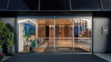 A hotel entrance with a glass door, a reception desk, and a seating area visible through the glass.