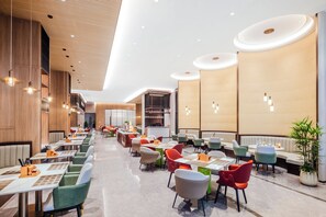 A modern restaurant interior with multiple dining tables and chairs, a bar area, and a kitchen in the background.