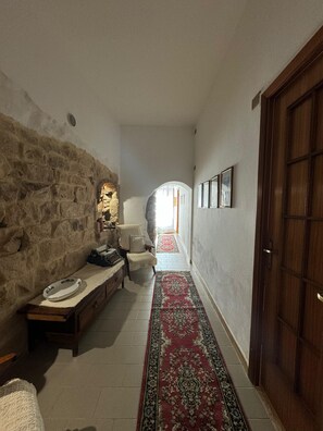 A hallway with a stone wall, a wooden door, a bench with a rug, and a corridor leading to a bright room. - Domu 'e ajiajius Vacation Home (Gonnesa)