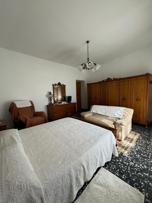 A bedroom with a large bed, a wooden wardrobe, a chair, and a desk with a mirror. - Domu 'e ajiajius Vacation Home (Gonnesa)