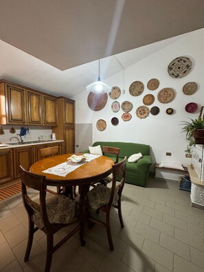 Uma sala de jantar com mesa e cadeiras de madeira, um sofá verde e uma parede decorada com vários pratos trançados.