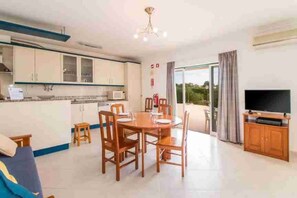 A modern kitchen with a dining area, a flat-screen TV, and a balcony with curtains. - 4 Bedroom Villa Lombos with Pool in Porches (Lagoa)