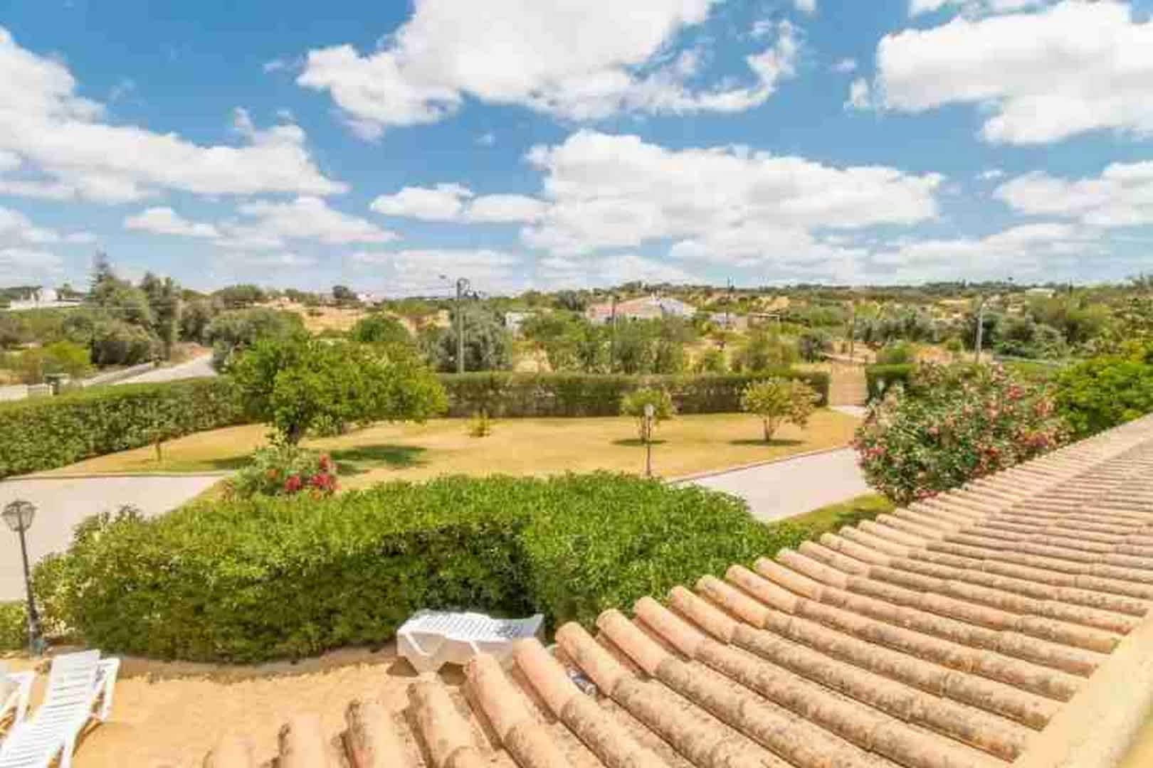 A rooftop terrace with a view of a landscaped garden, a paved walkway, and a distant town.