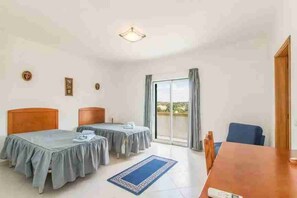 A hotel room with two beds, a dining table, a view through a sliding glass door, and a ceiling light fixture. - 4 Bedroom Villa Lombos with Pool in Porches (Lagoa)