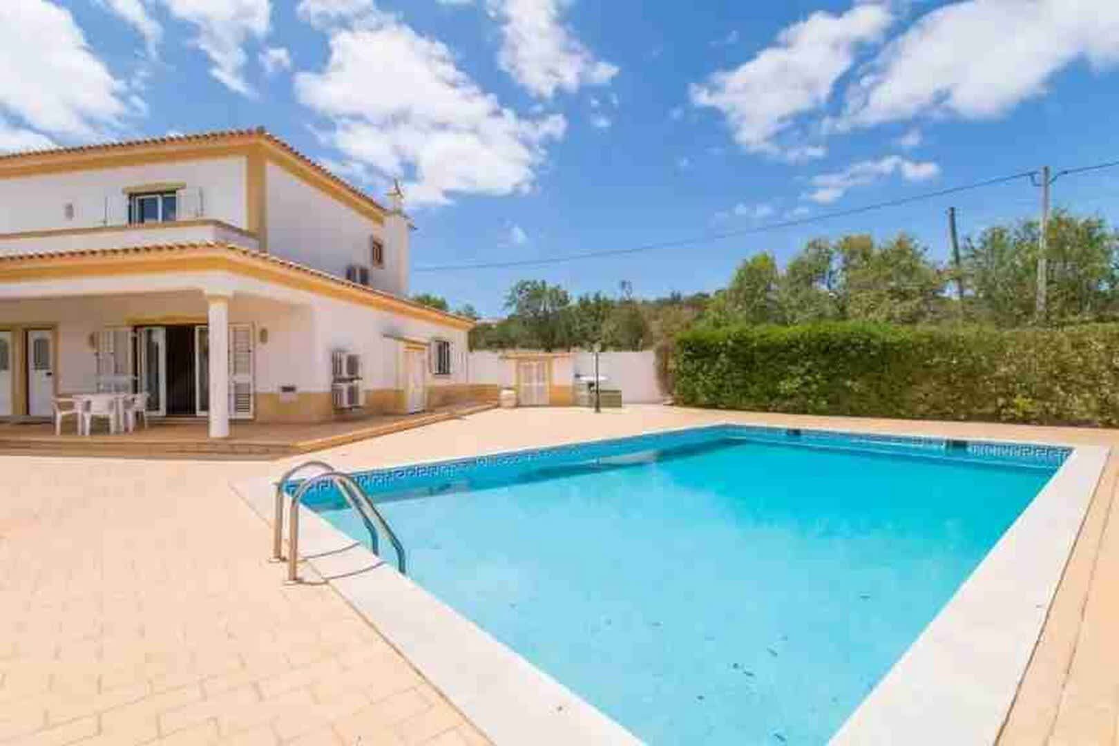 A two-story house with a swimming pool, outdoor furniture, and a clear sky.