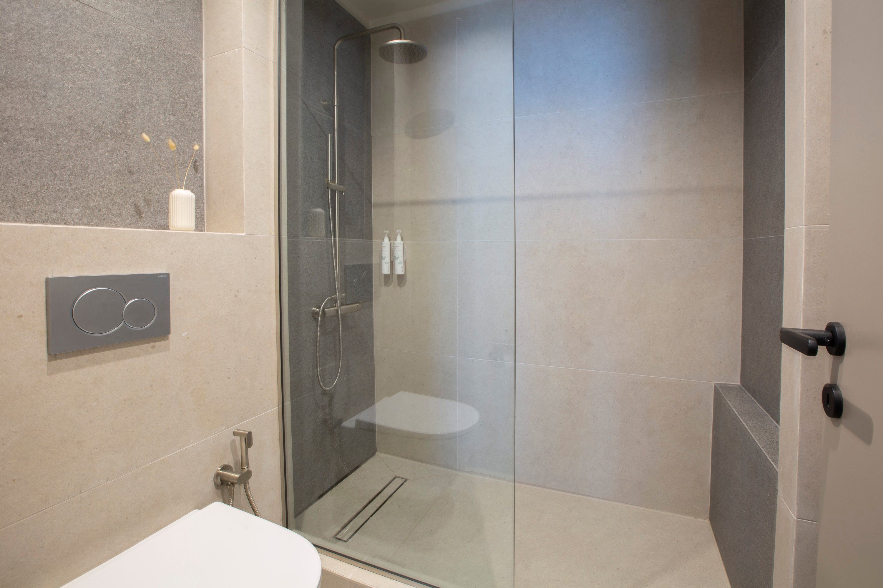 A modern bathroom with a glass-enclosed shower, a toilet, and a sink.