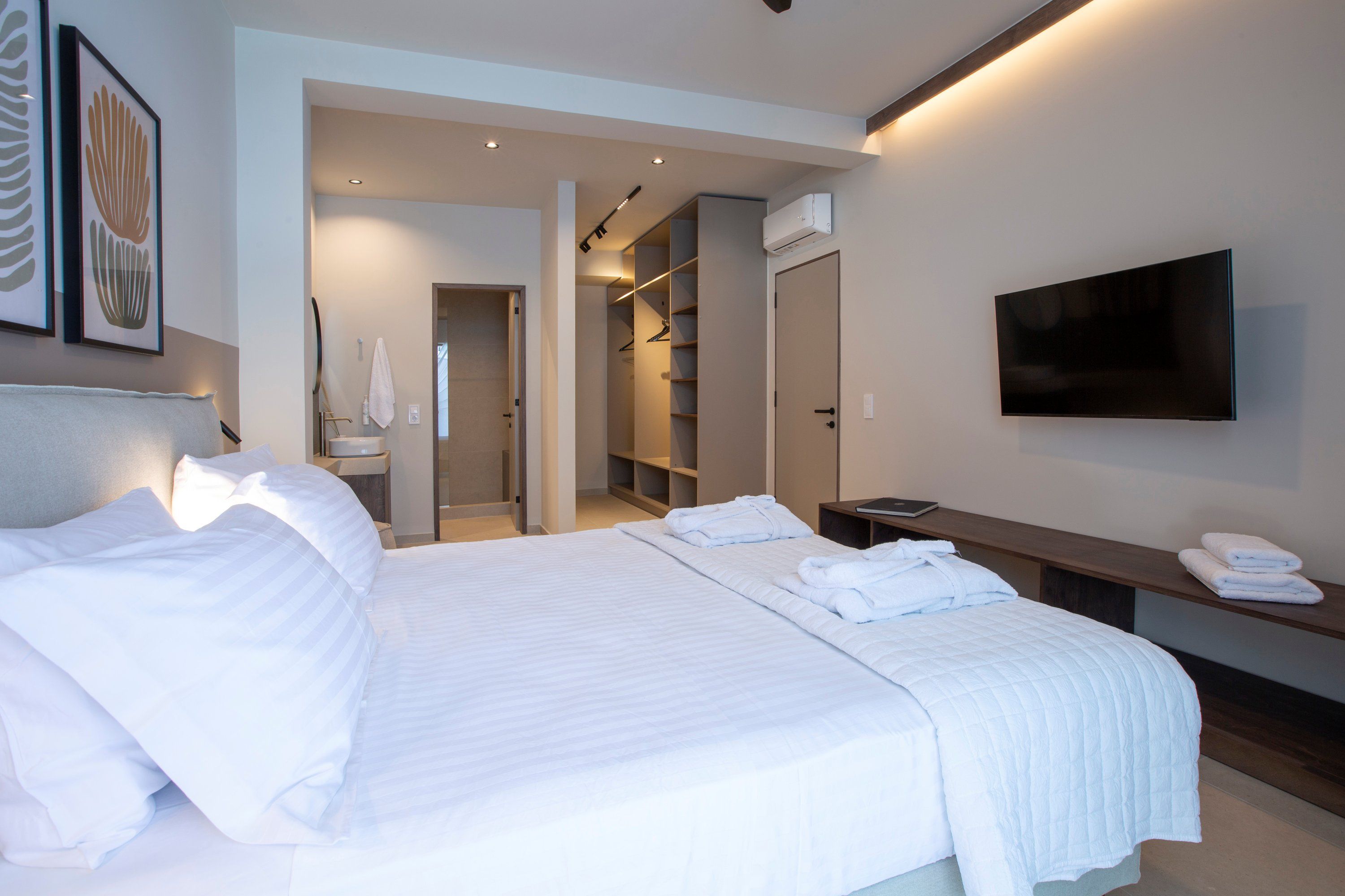A modern hotel room with a large bed, a TV mounted on the wall, and a walk-in closet.