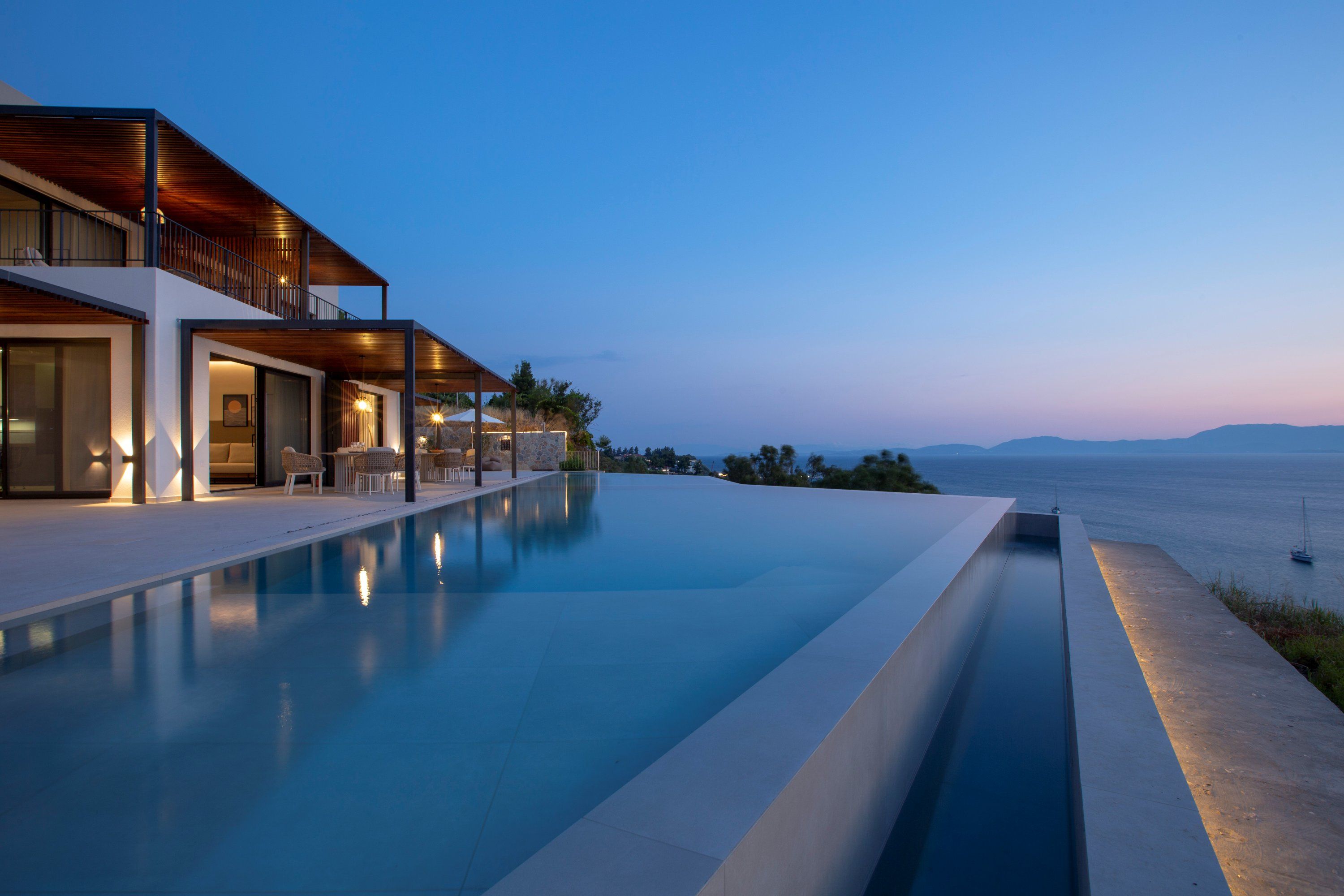 A modern house with a swimming pool, outdoor seating, and a view of the sea.