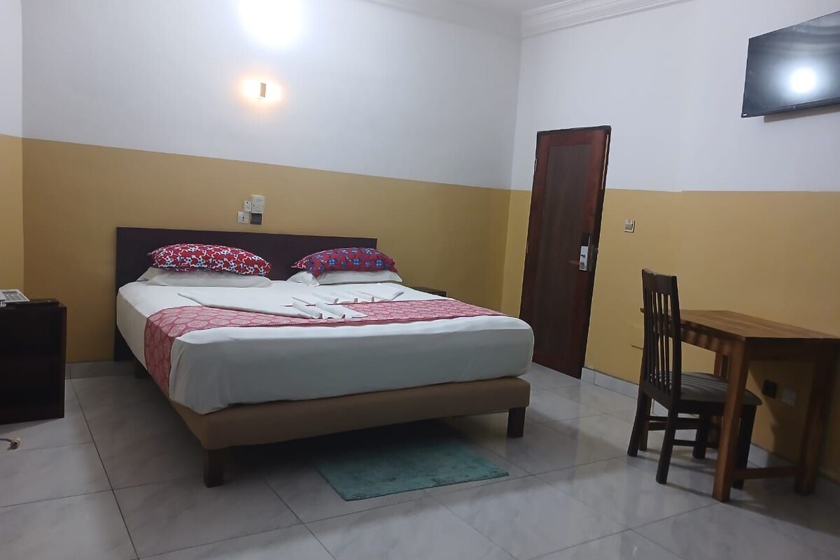 Quarto com cama, mesa de cabeceira, cadeira e televisão na parede.