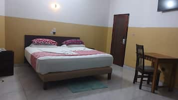 A bedroom with a bed, bedside table, chair, and a television on the wall.