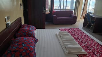 Una habitación de hotel con cama, sofá, escritorio y vistas al mar a través de amplios ventanales.