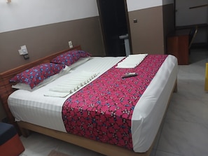 Cama com colcha estampada em branco e vermelho, um travesseiro e um controle remoto.