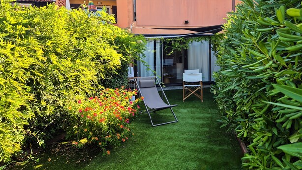 En välskött trädgård med en gräsmatta, en sittplats med en stol och en byggnad med en glasdörr.